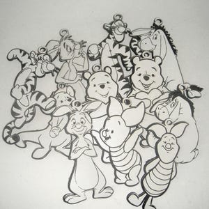 May include: A collection of black and white cartoon character cutouts, including Winnie the Pooh, Tigger, Piglet, Eeyore, and Rabbit. Each character has a small loop at the top, suggesting they are designed to be hung or used as charms.