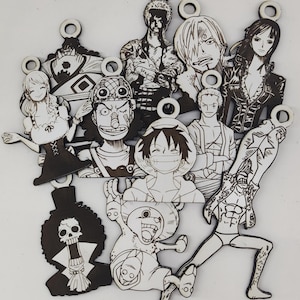 May include: A collection of wooden cutouts featuring characters from the anime series One Piece. Each cutout is black and white, depicting various characters with distinct facial expressions and outfits. The cutouts have a small hole at the top for hanging.