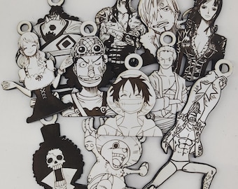 May include: A collection of wooden cutouts featuring characters from the anime series One Piece. Each cutout is black and white, depicting various characters with distinct facial expressions and outfits. The cutouts have a small hole at the top for hanging.