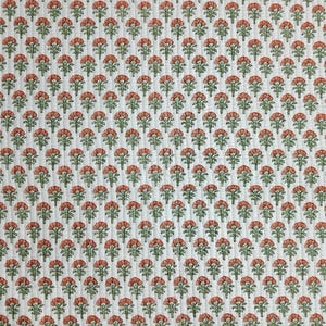 May include: A white quilted fabric featuring a repeating pattern of small, stylized orange flowers with green stems and leaves. The textile has vertical stitching lines running throughout, creating a textured, grid-like appearance across the surface.