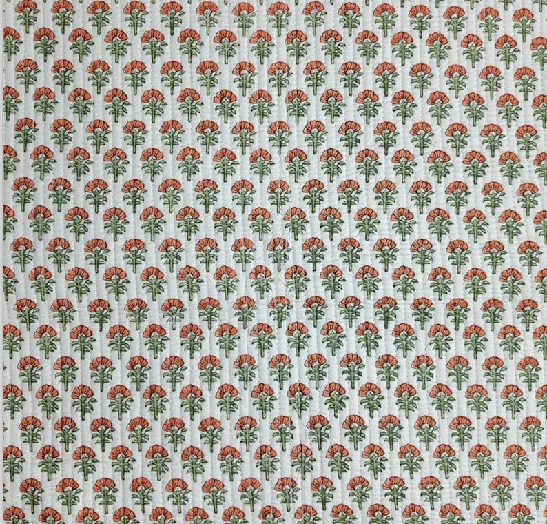 May include: A white quilted fabric featuring a repeating pattern of small, stylized orange flowers with green stems and leaves. The textile has vertical stitching lines running throughout, creating a textured, grid-like appearance across the surface.