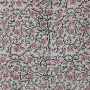 May include: A white fabric featuring a repeating floral pattern with pink blossoms and green vines. The material has a visible quilted texture with fine, parallel stitching lines running vertically across the entire surface of the textile.