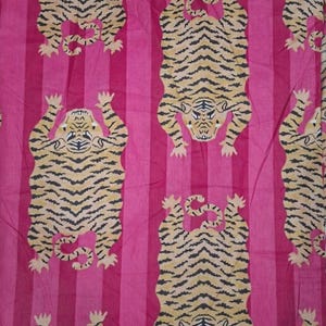May include: A fabric featuring a repeating pattern of tan tigers with black stripes arranged in a vertical layout. The background consists of alternating vertical stripes in two distinct shades of pink, creating a vibrant and consistent textile design.