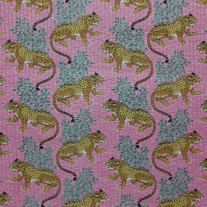 May include: A pink fabric featuring a repeating pattern of yellow and black spotted leopards interspersed with green leafy foliage. The textile has a visible quilted texture with fine stitching lines running across the entire surface.
