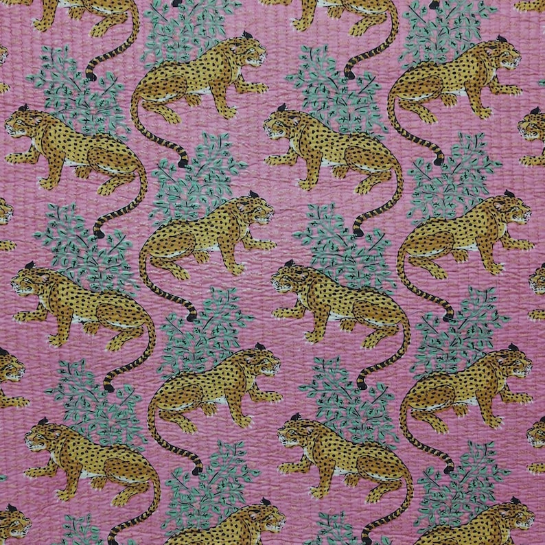 May include: A pink fabric featuring a repeating pattern of yellow and black spotted leopards interspersed with green leafy foliage. The textile has a visible quilted texture with fine stitching lines running across the entire surface.