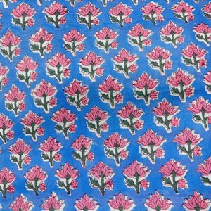 May include: A light blue fabric featuring a repeating pattern of pink lotus flowers with green stems and leaves. The floral design is evenly spaced across the surface, creating a consistent botanical print on the blue textile background.