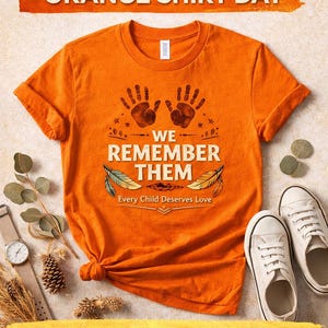 May include: Bright orange t-shirt featuring the text "WE REMEMBER THEM" and "Every Child Deserves Love." The design includes handprints and feather graphics. The words "PHYSICAL ITEM - ORANGE SHIRT DAY" and "PHYSICAL T-SHIRT" are also visible.