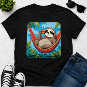 May include: Black t-shirt with a cartoon sloth in a hammock, holding a coffee mug. The sloth is brown and tan, with a black eye mask. The hammock is red, and the background is blue with green palm leaves. Text reads "Livin' the Sloth Life."