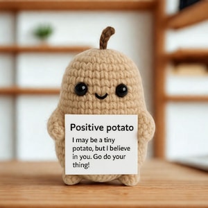 Op de afbeelding: Een beige gehaakte aardappel figuur met een lachend gezicht en zwarte knoopogen. Het houdt een bord vast met de tekst "Positive potato. I may be a tiny potato, but I believe in you. Go do your thing!"