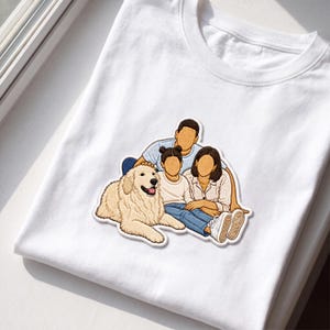 May include: A white t-shirt featuring a central embroidered patch depicting a family of three and a large golden-colored dog. The figures have no facial features. The group includes a person in a light blue shirt, a child, and another adult.