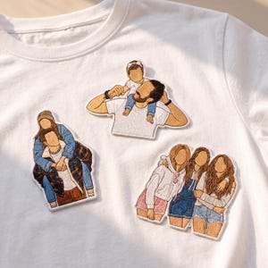 May include: A white t-shirt featuring three distinct embroidered patches. One patch shows a person carrying a child on their shoulders, another depicts a person giving a piggyback ride, and the third shows three individuals standing side by side.
