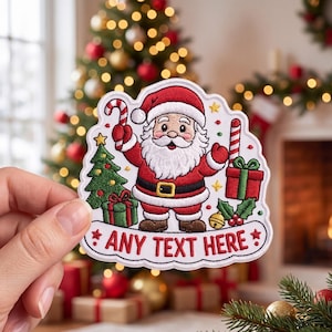 May include: An embroidered patch featuring a cartoon Santa Claus in a red suit, a green Christmas tree with gifts, a candy cane, and holly. The patch has a white border and a banner at the bottom with the red embroidered text ANY TEXT HERE.