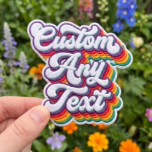 May include: An embroidered patch featuring the white text Custom Any Text in a bold, retro script font. The lettering is layered over a vibrant, multi-colored background consisting of concentric wavy stripes in purple, red, orange, and green.