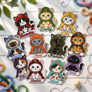 May include: A collection of twelve cat stickers, each wearing a hooded cape featuring a different zodiac symbol. The cats are illustrated in a cartoon style with names like Tommy, Emily, Lily, Daisy, Ava, Madison, Jack, Olivi, Sophia, and Chloe printed below.