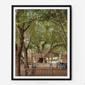 May include: A wooden playground structure with a tower and a slide, surrounded by lush green trees. Several bicycles are parked nearby.