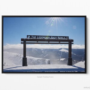 May include: A wooden sign with the text "THE LEGENDARY BACK BOWLS" in white letters against a blue sky. The sign is a gateway to a snowy mountain landscape.