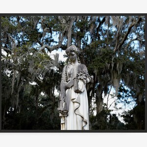 May include: A white stone statue of a woman with long hair, standing in a forest with moss-covered trees. The statue is wearing a long dress and holding a bouquet of flowers.