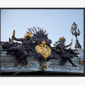 Puede incluir: Primer plano de una barandilla de puente decorativa con dos estatuas negras que sostienen antorchas, un escudo de armas dorado y una farola negra con detalles dorados.