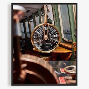 May include: A close-up of a brass ship's wheel with a black face and white markings. The wheel is labeled "Stop by Stand" and has markings for "Slow", "Half", "Full", "Astern", and "Ahead".