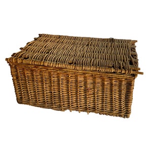 May include: A large, rectangular wicker basket with a woven lid. The basket is made of natural brown wicker and has a rustic, vintage look.