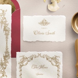 May include: Elegant wedding stationery set featuring a cream-colored place card with the name "Olivia Smith" and a menu card with the text "The Menu". Both cards have gold ornate designs and are on a textured surface.