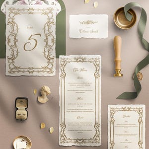 May include: Elegant wedding stationery set featuring a table number, menu, and place card with ornate gold filigree borders. Includes a ring box, wax seal, and a small bust. The envelope has a floral design.