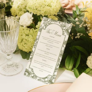May include: A menu card with a floral design and the words "The Menu" at the top. The menu lists starters, mains, and desserts. A clear wine glass and floral arrangement are in the background.