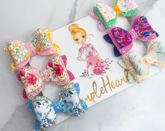 May include: Set of 6 floral print hair bows with glitter accents. The bows are in various colors, including pink, blue, green, and yellow. The bows are arranged on a white background with the text "SimpleHeart".