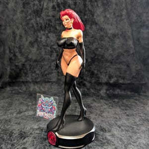 May include: A detailed figurine of a woman with red hair, wearing a black outfit, including a top, underwear, gloves, and thigh-high stockings. The figure is standing on a black base with a red accent. The Printmaster logo is visible.