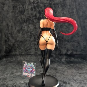 May include: A figurine of a woman with long, flowing red hair, wearing a black lingerie set and thigh-high stockings. The figure is standing on a black circular base. A sticker with the text "PRINTMASTER" is visible.