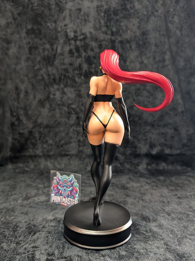 May include: A figurine of a woman with long, flowing red hair, wearing a black lingerie set and thigh-high stockings. The figure is standing on a black circular base. A sticker with the text "PRINTMASTER" is visible.