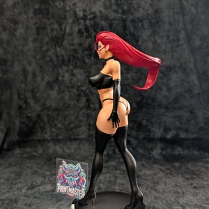 May include: A figurine of a woman with long red hair, wearing a black outfit, including a top, gloves, and thigh-high stockings. The figure is posed on a black circular base. The figurine has a detailed design and is a collectible item.