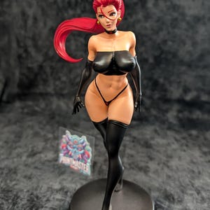 May include: A detailed figurine of a woman with red hair, wearing a black top, gloves, and thigh-high stockings. The figure is posed on a round base, with a small logo visible near the base. The figurine has a detailed design.
