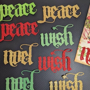 May include: Assortment of glitter-covered paper cutouts with the words "peace", "wish", and "Noel" in various colors, including red, green, and gold.