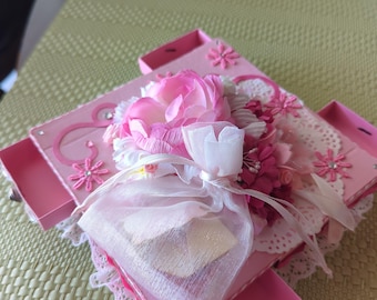 May include: A pink box with a white lace trim and a pink flower arrangement on top. The box has multiple compartments and is decorated with rhinestones.