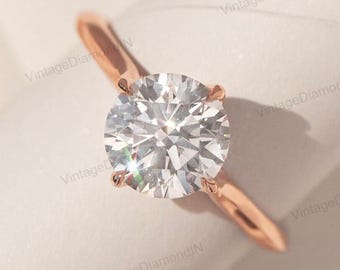 May include: A rose gold engagement ring featuring a large, round-cut diamond. The diamond is held in place by four prongs, and the band is a simple, polished design. The ring is set against a soft, neutral background.