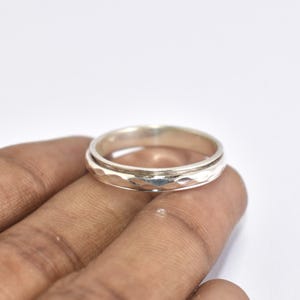 Peut inclure: Une bague en argent avec une bande texturée et un bord lisse surélevé. La bague est ronde et semble être faite d'un métal brillant. La bande présente un motif martelé ou facetté, ajoutant un intérêt visuel au bijou.