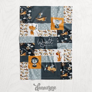 May include: A blue and gray baby blanket with a patchwork design featuring animals in airplanes. The blanket has the name "Wyatt Paul" in the center.