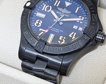 Könnte beinhalten: Eine schwarze Breitling Avenger Uhr mit dunkelblauem Zifferblatt sowie roségoldfarbenen Ziffern und Zeigern. Die Uhr verfügt über ein Datumsfenster auf der Drei-Uhr-Position, eine drehbare Lünette mit eingravierten Markierungen und ein schwarzes Metallarmband.