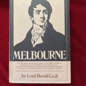 May include: A book cover with a black and white illustration of a man in a suit. The title of the book is "MELBOURNE" and the author is "Lord David Cecil".