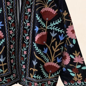 May include: A dark navy blue embroidered jacket with floral patterns. The jacket features intricate embroidery in shades of pink, red, blue, and gold. The design includes stylized flowers and leaves, creating a bohemian aesthetic.
