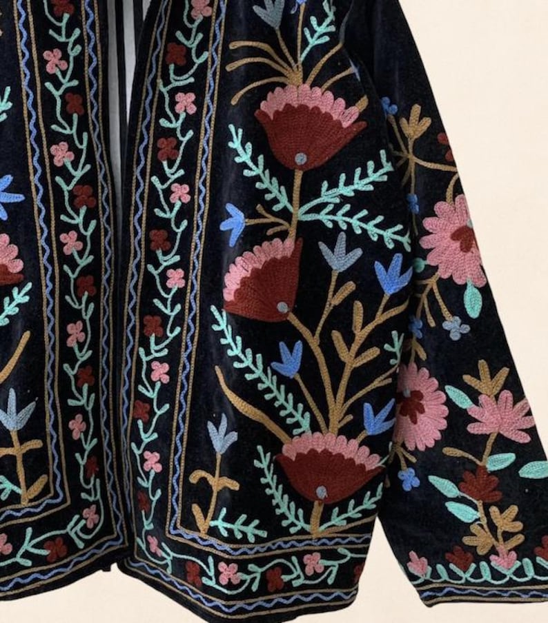 May include: A dark navy blue embroidered jacket with floral patterns. The jacket features intricate embroidery in shades of pink, red, blue, and gold. The design includes stylized flowers and leaves, creating a bohemian aesthetic.