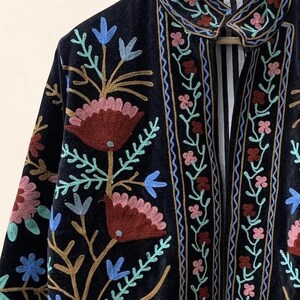 May include: A dark navy blue embroidered jacket with a floral design. The jacket features a collar and is adorned with colorful embroidered flowers in shades of red, pink, blue, and green. The interior lining has a striped pattern.