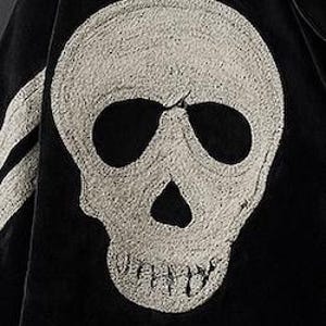 May include: Close-up of a black jacket featuring a large, textured, off-white skull emblem on the front. The skull has prominent eye sockets and a detailed jawline. A white stripe is visible on the left side of the jacket.