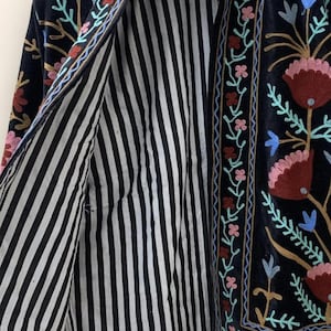 May include: A dark navy blue jacket with floral embroidery in pink, red, blue, and yellow. The jacket's interior features black and white vertical stripes. The embroidery is along the edges and collar.