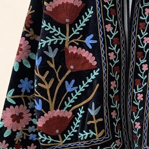 May include: Black velvet jacket with colorful floral embroidery. The embroidery features shades of red, pink, blue, and gold. The jacket has a detailed border design and a flowing, open front.