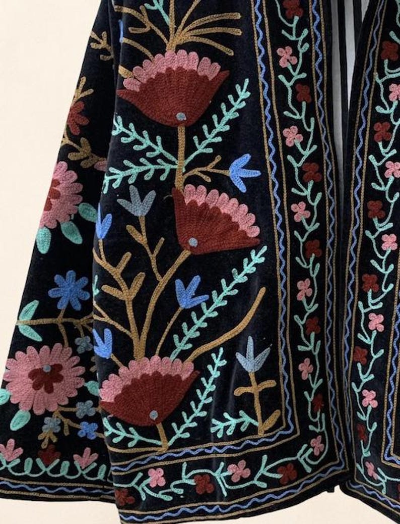 May include: Black velvet jacket with colorful floral embroidery. The embroidery features shades of red, pink, blue, and gold. The jacket has a detailed border design and a flowing, open front.