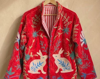 May include: A red velvet jacket with white rabbit embroidery and floral accents. The jacket features a striped lining and is displayed on a wooden hanger. The embroidery includes blue, green, and gold details.