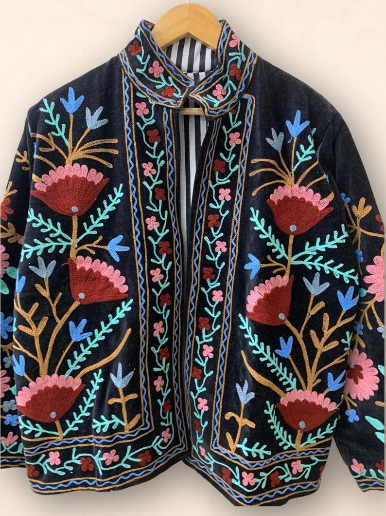 May include: Black velvet jacket with colorful floral embroidery. The jacket features a collar and a striped lining. The embroidery includes red, pink, blue, and gold thread, creating a vibrant and detailed design.