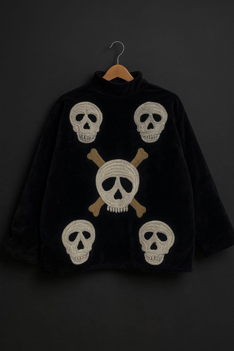 May include: Black turtleneck sweater with embroidered skull and crossbones design. The sweater features five embroidered skulls in a cream color, with a larger skull and crossbones in the center. The sweater is hanging on a wooden hanger.